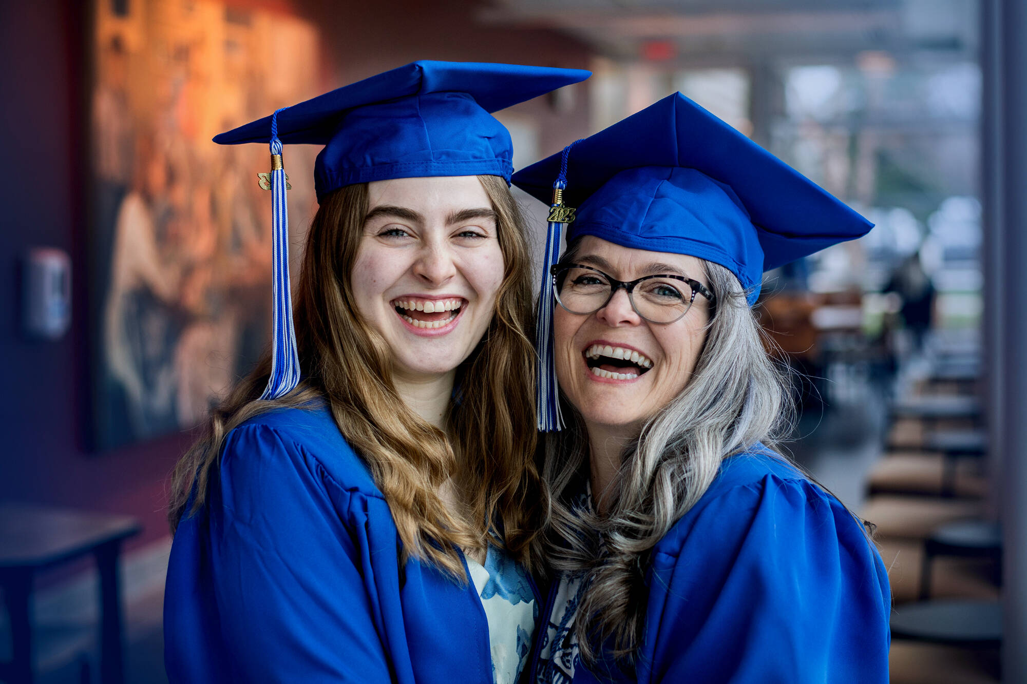 Two graduates in blue caps and gowns, one older, one younger